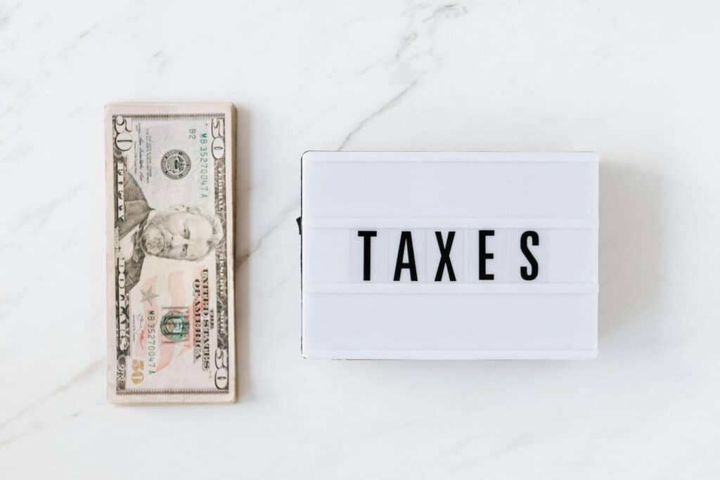 Master Your Finances with the Best Tax Planner for Every Need 2 Overhead view of a fifty-dollar bill and a lightbox with 'TAXES' on a marble surface.