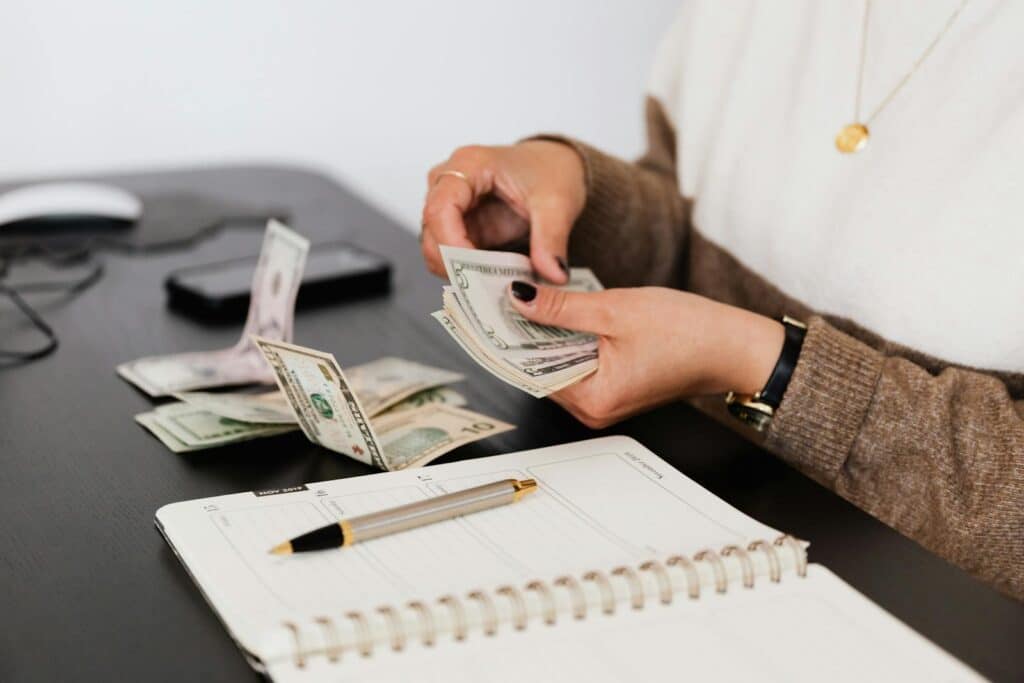 Close-up of person counting cash with notepad on desk, indicating financial tasks. forensic accounting