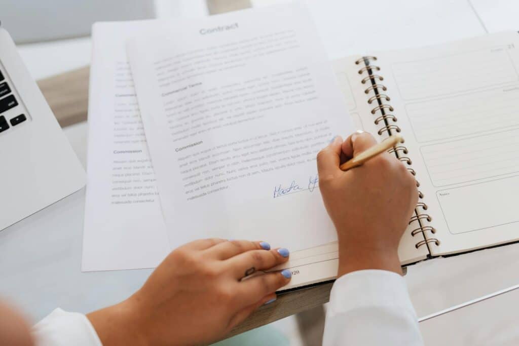 Close-up of hands signing a contract on a desk with office supplies, symbolizing legal agreements. what is a slat
