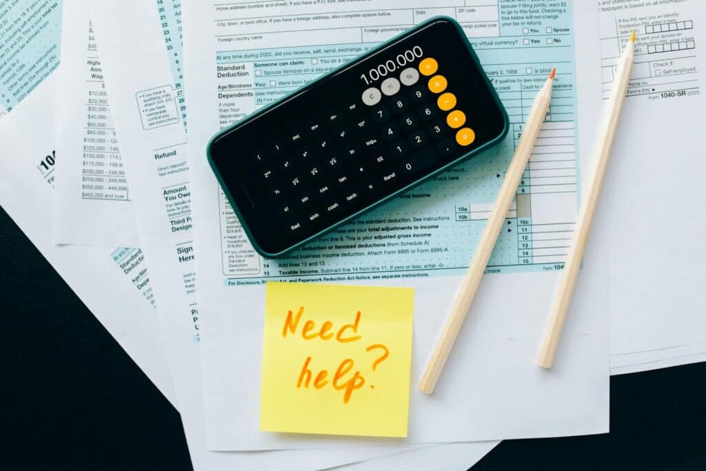 Top view of financial papers with a calculator, pencils, and a note saying 'Need help?' indicating tax or accounting assistance. cost accounting